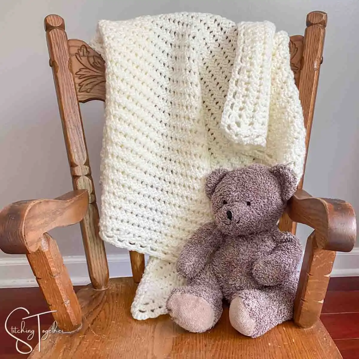 crochet lacy baby blanket draped on chair with stuffed bear next to it