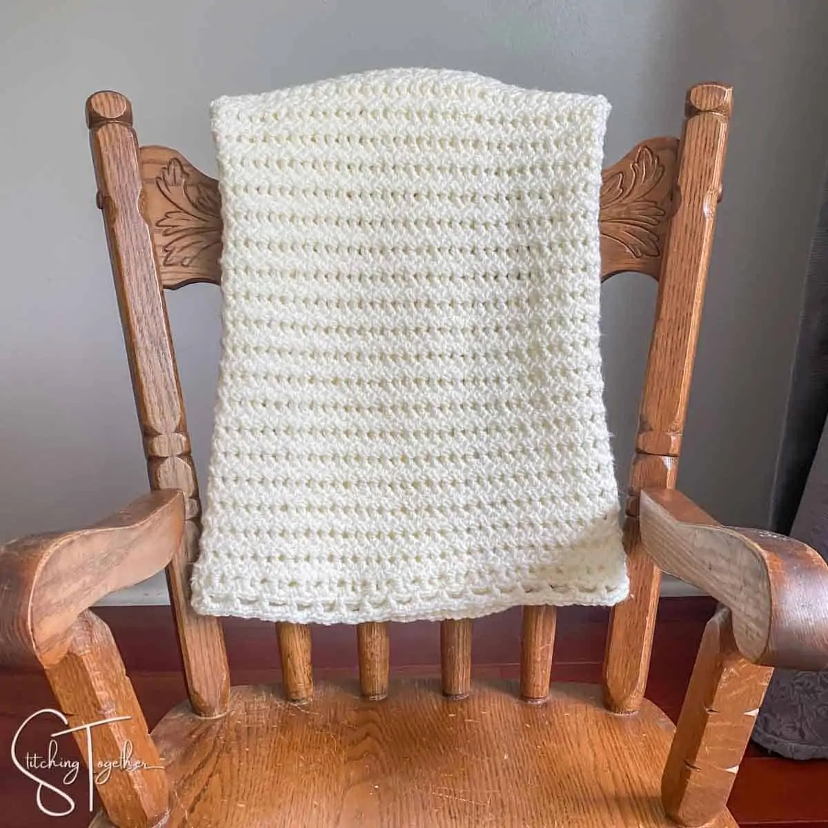 light and lacy crochet baby blanket draped over the back of a small rocking chair