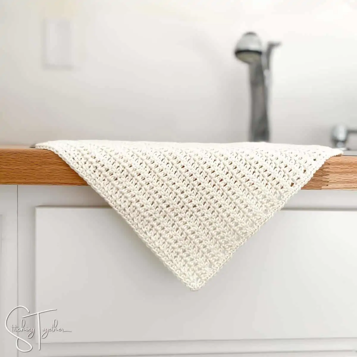 cream crochet dishcloth hanging over the side of the sink