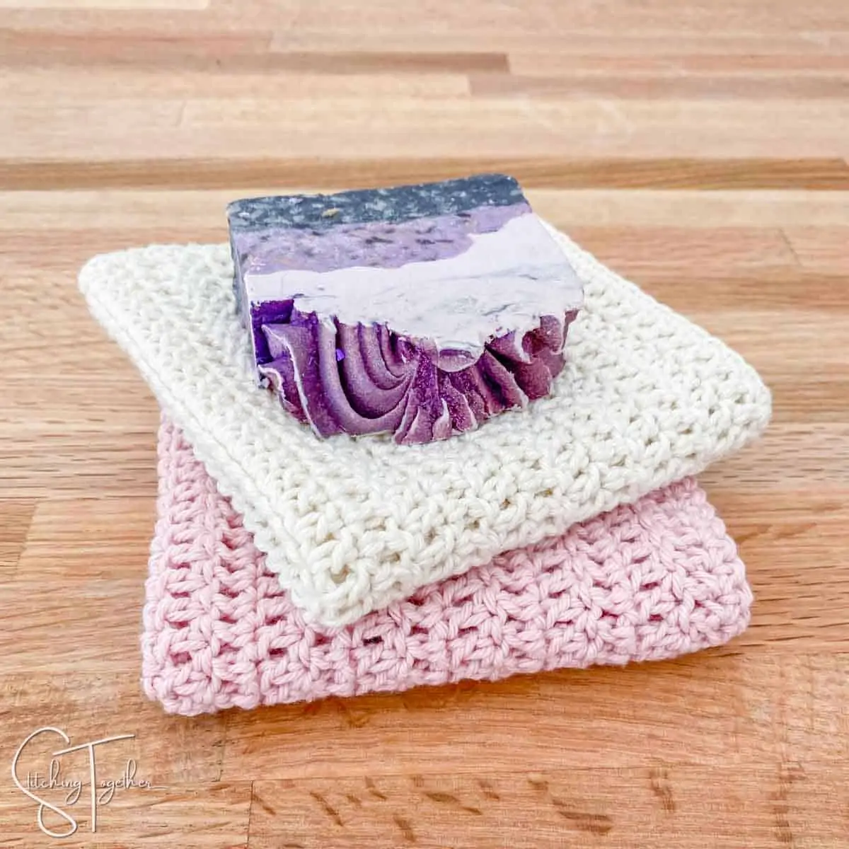 two folded easy double crochet dishcloths with a bar of soap on top