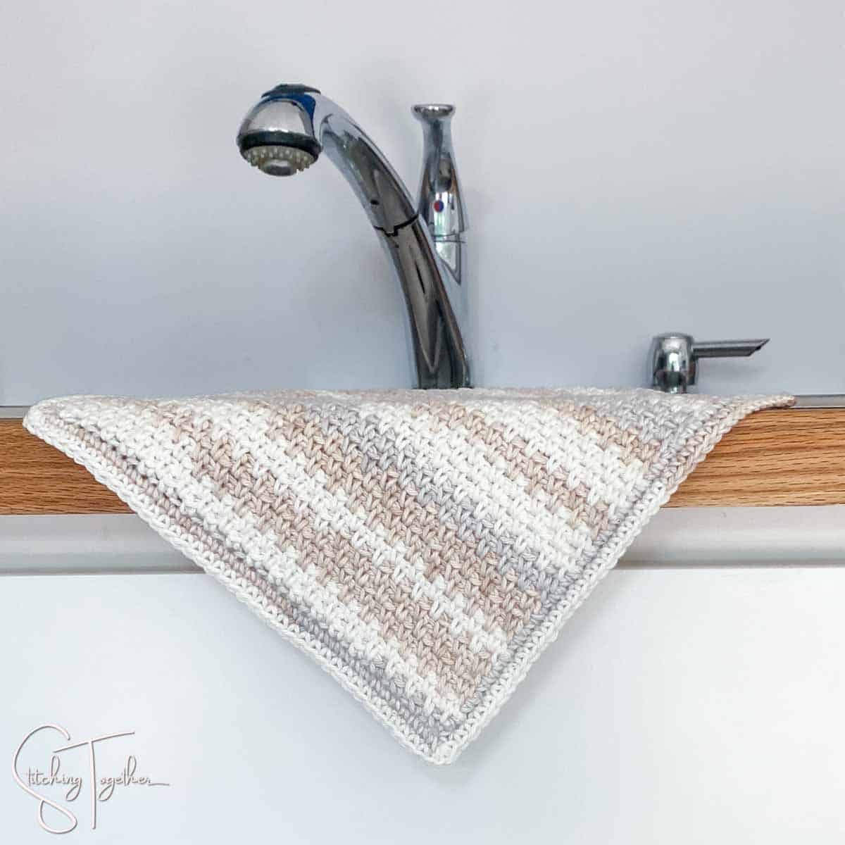 striped moss stitch dishcloth hanging over the side of a counter