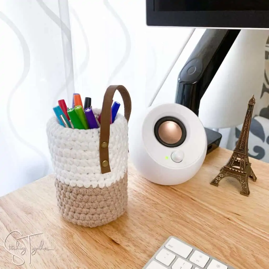 crochet pen holder filled with colorful pens sitting on a desk next to a small speaker