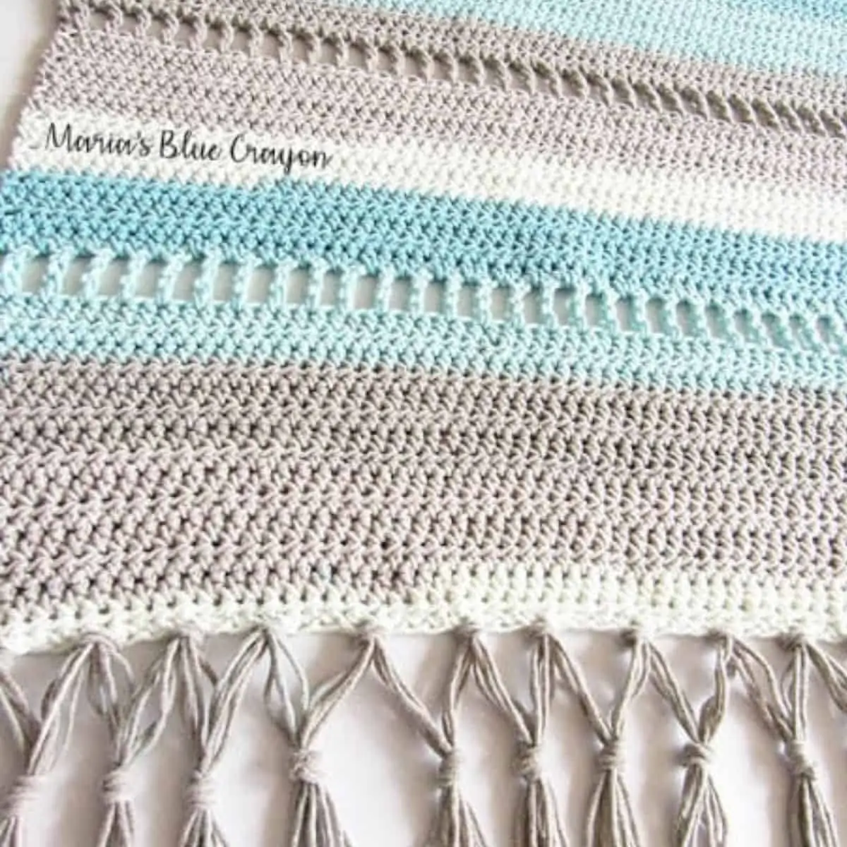 close up of gray, tan, light blue striped crochet rug with fringe