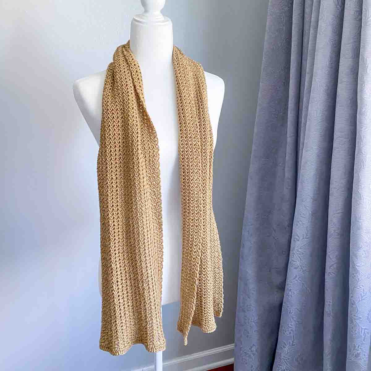 flowy crochet scarf in a yellow golden color draped on the shoulders of a mannequin