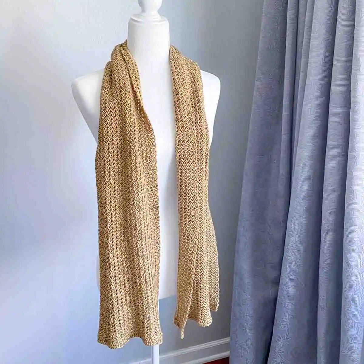 flowy crochet scarf in a yellow golden color draped on the shoulders of a mannequin