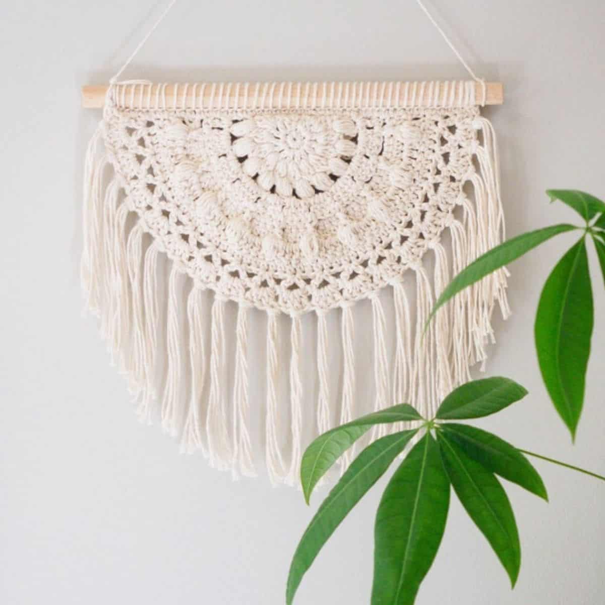 decoração de parede em crochê boho semicírculo com parte de uma planta na frente