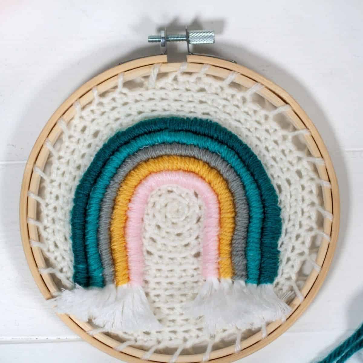 pequeno arco-íris de crochê e fios em um bastidor de bordar.