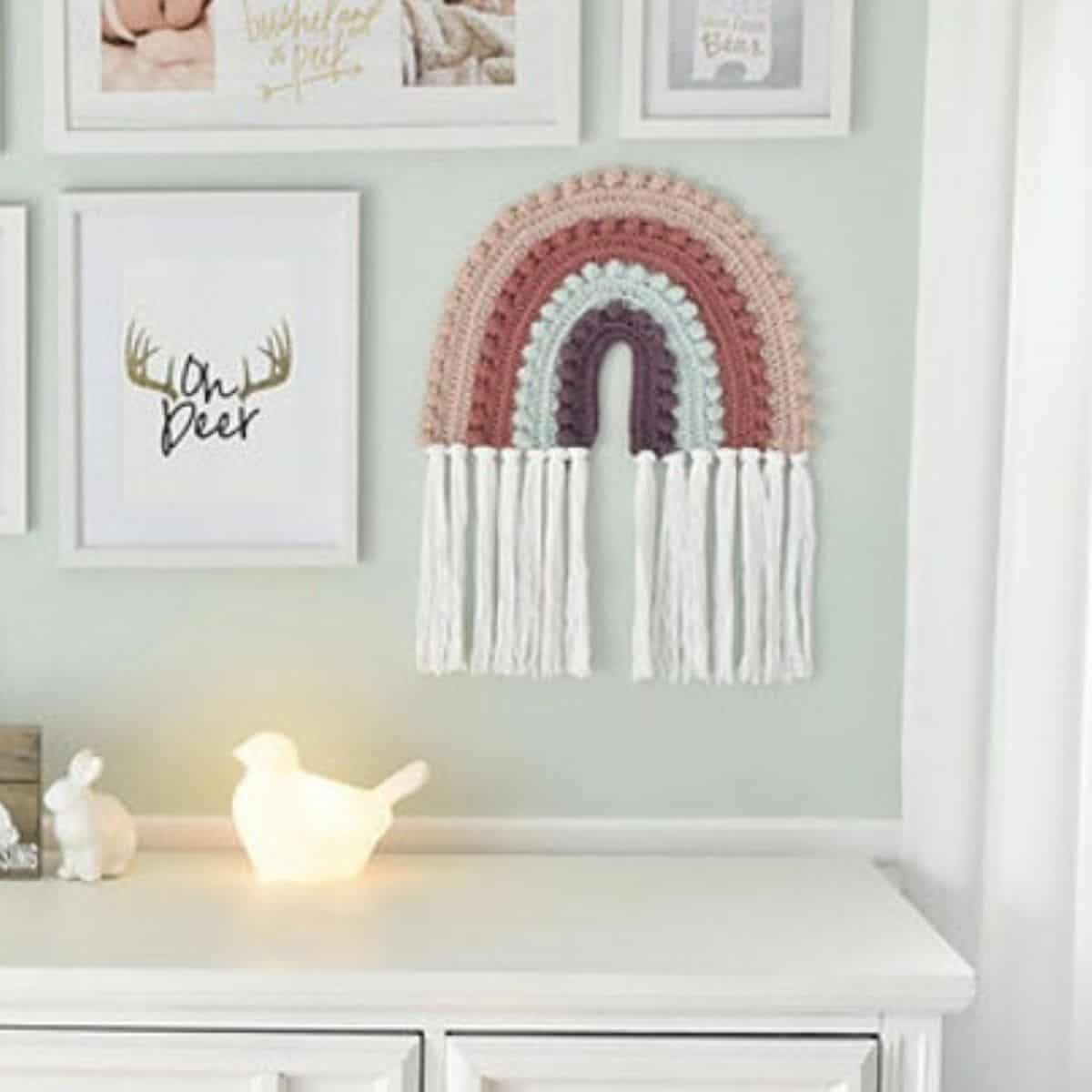 parede do berçário decorada com estampas e um grande arco-íris pendurado em crochê