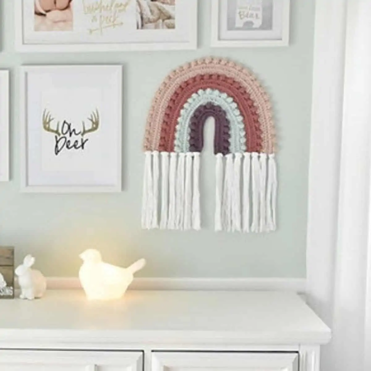 nursery wall decorated with prints and a large crochet rainbow hanging