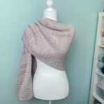 neutral modern crochet shawl with one side draped over the shoulder of a mannequin