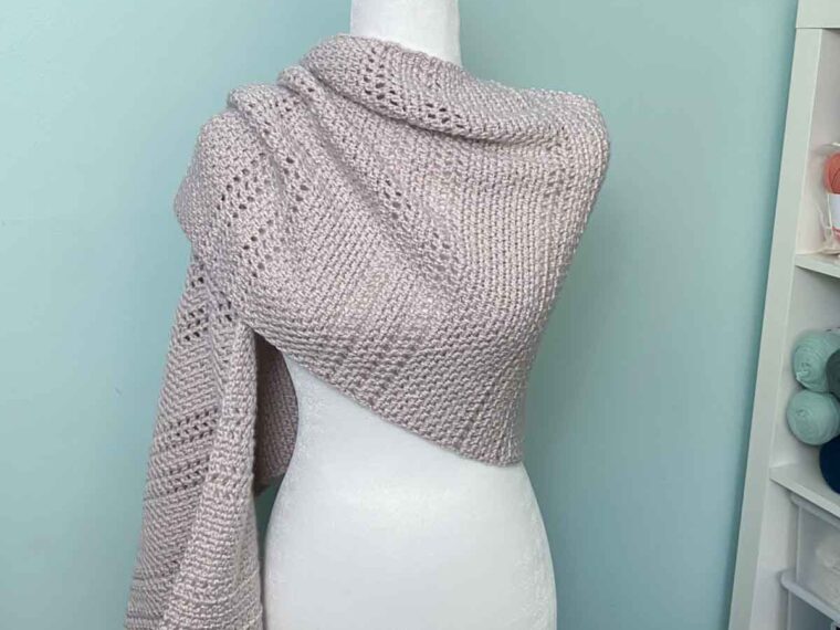 neutral modern crochet shawl with one side draped over the shoulder of a mannequin