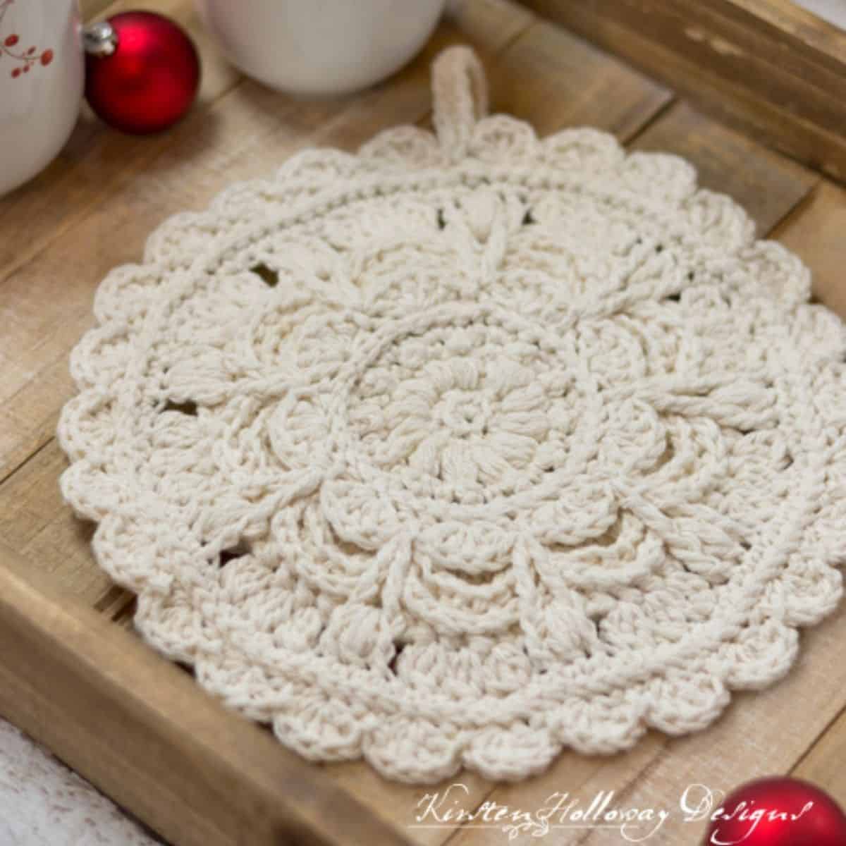 an intricate ivory crochet round hot pad sitting on a wooden tray