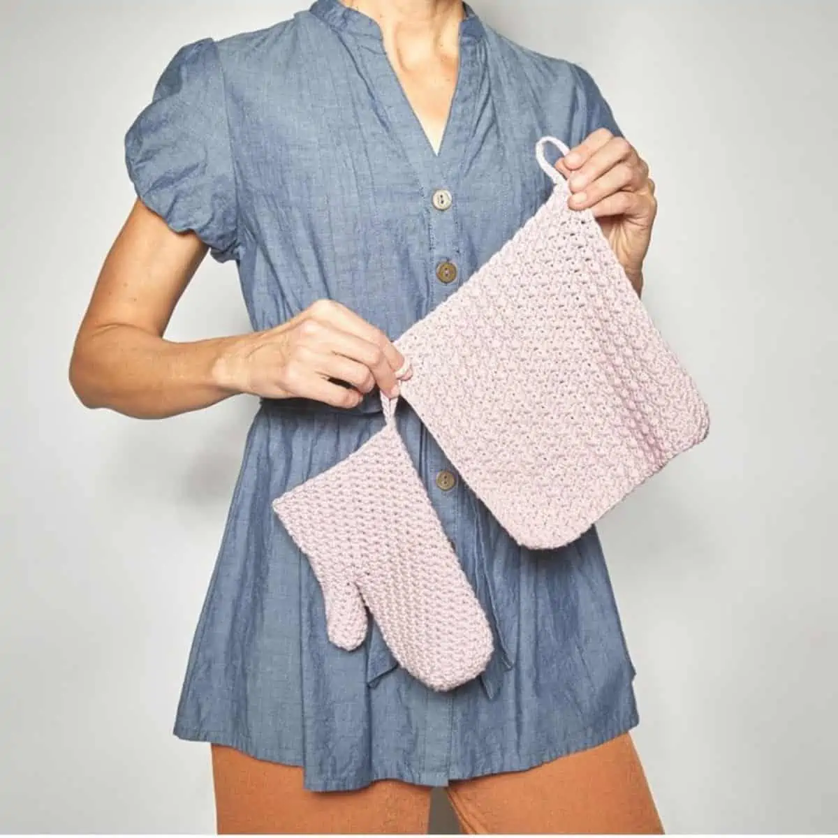 woman holding a pink crochet oven mitt and potholder