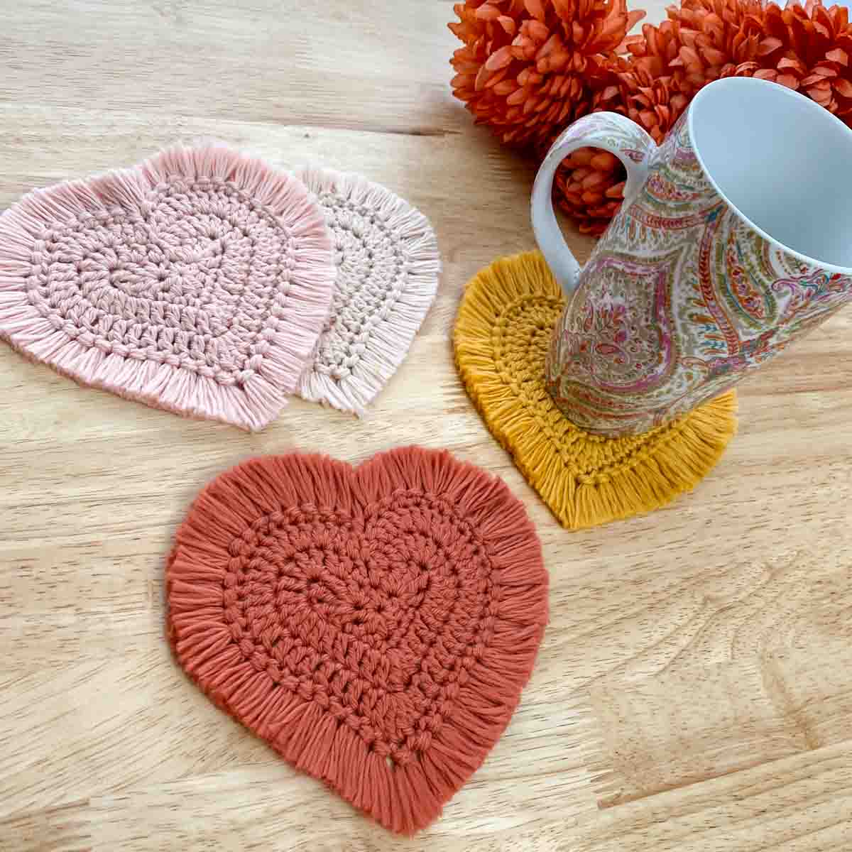 a colorful mug sitting on a crochet heart coaster with other crochet hearts sitting nearby
