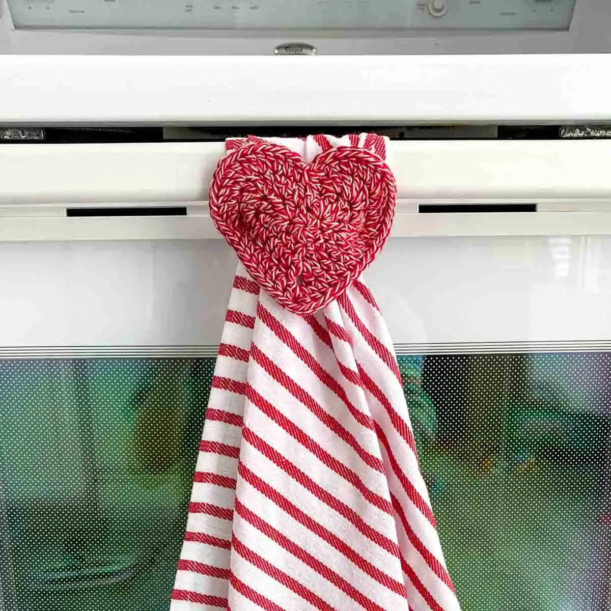 red and white striped tea towel with a crochet heart hanger hanging on an oven handle