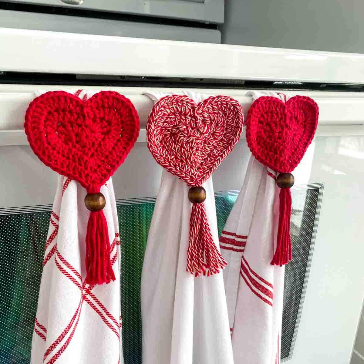 3 heart crochet tea towel toppers hanging 3 red and white towels on a oven handle