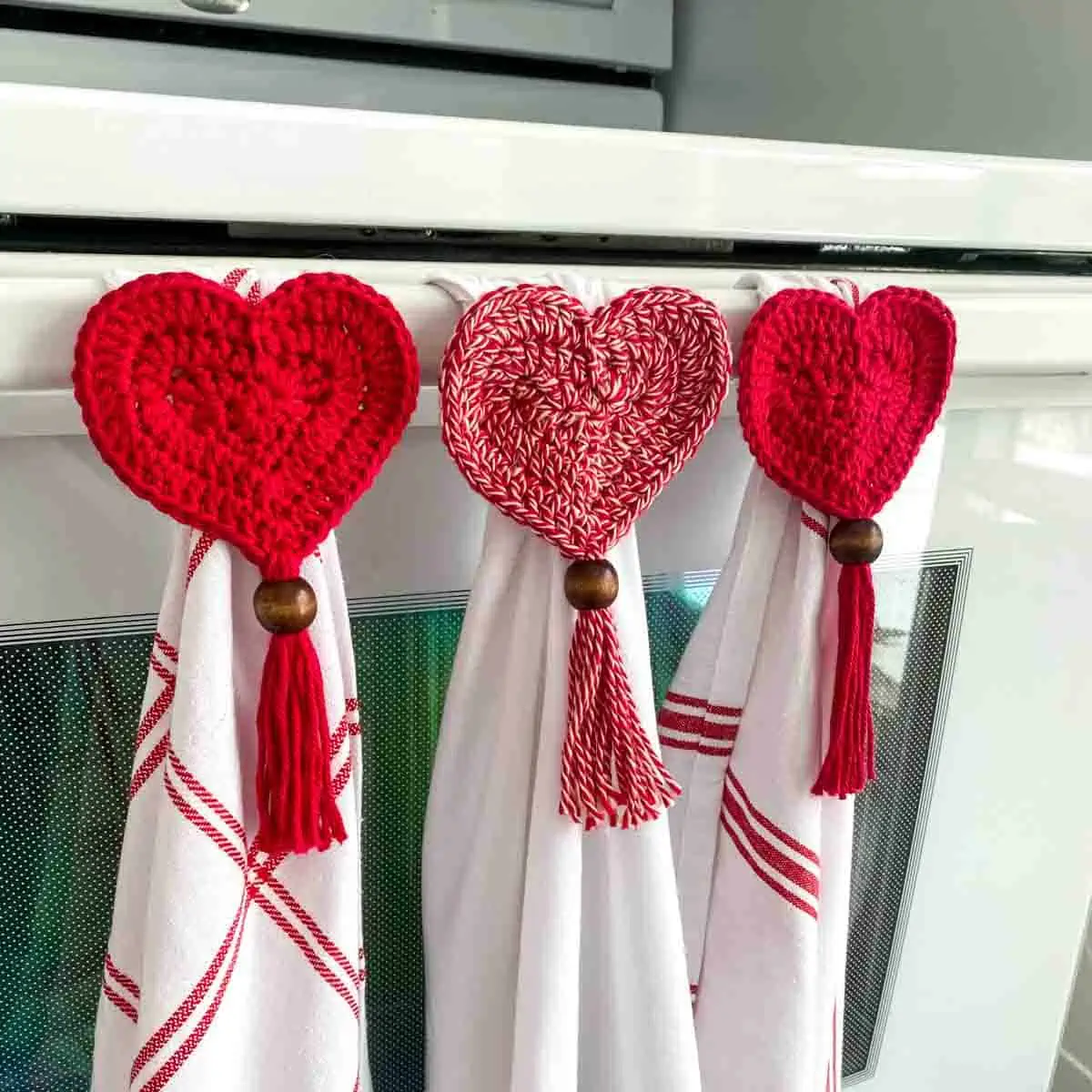 3 heart crochet tea towel toppers hanging 3 red and white towels on a oven handle