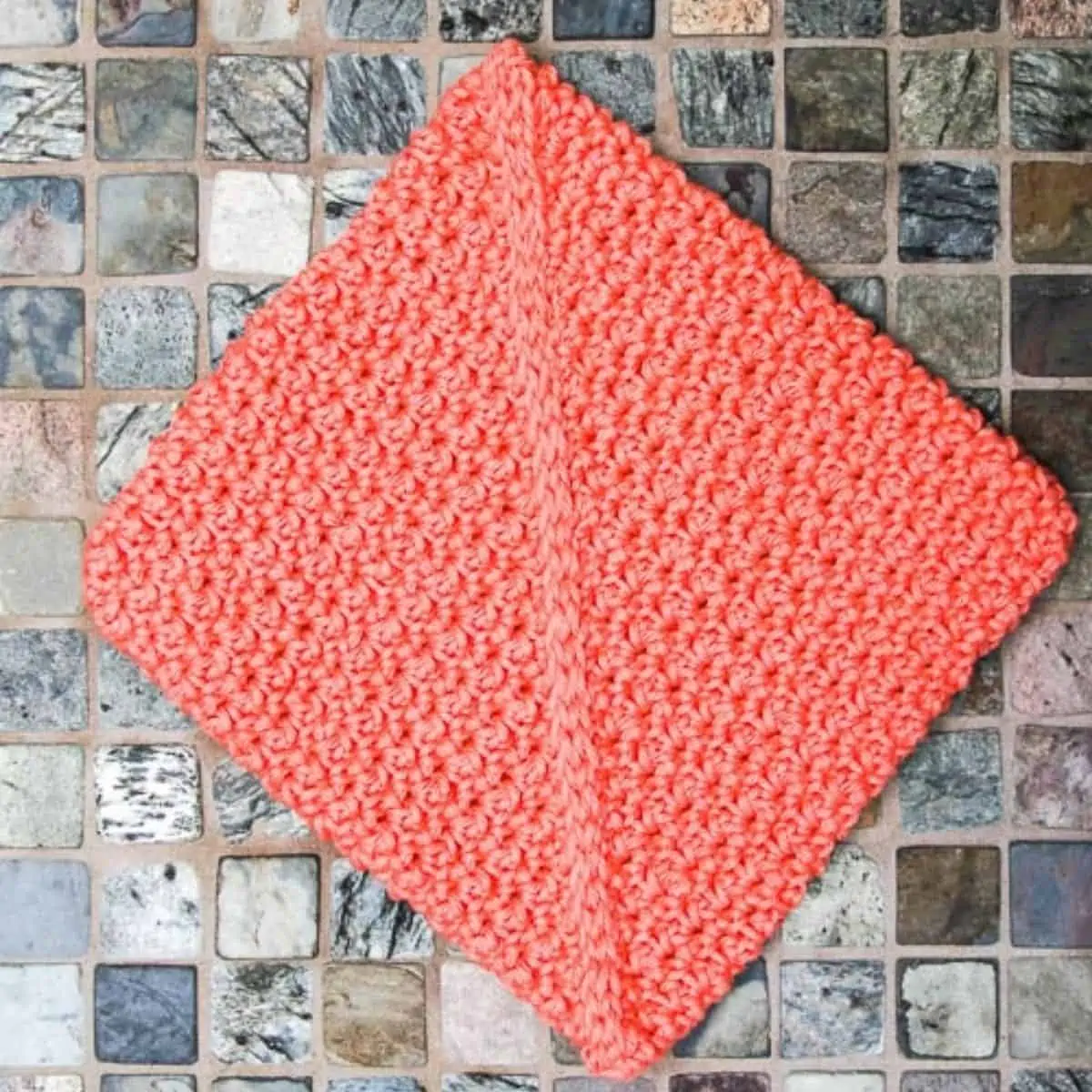 coral colored crochet potholder with a seam down the middle laying flat on tile