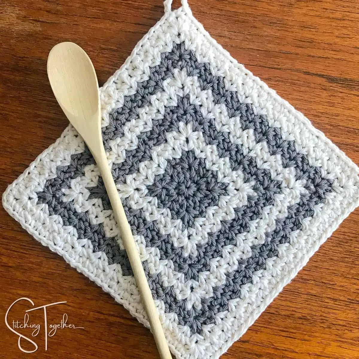 gray and white striped hot pad laying on a table with a wooden spoon laying on top of it