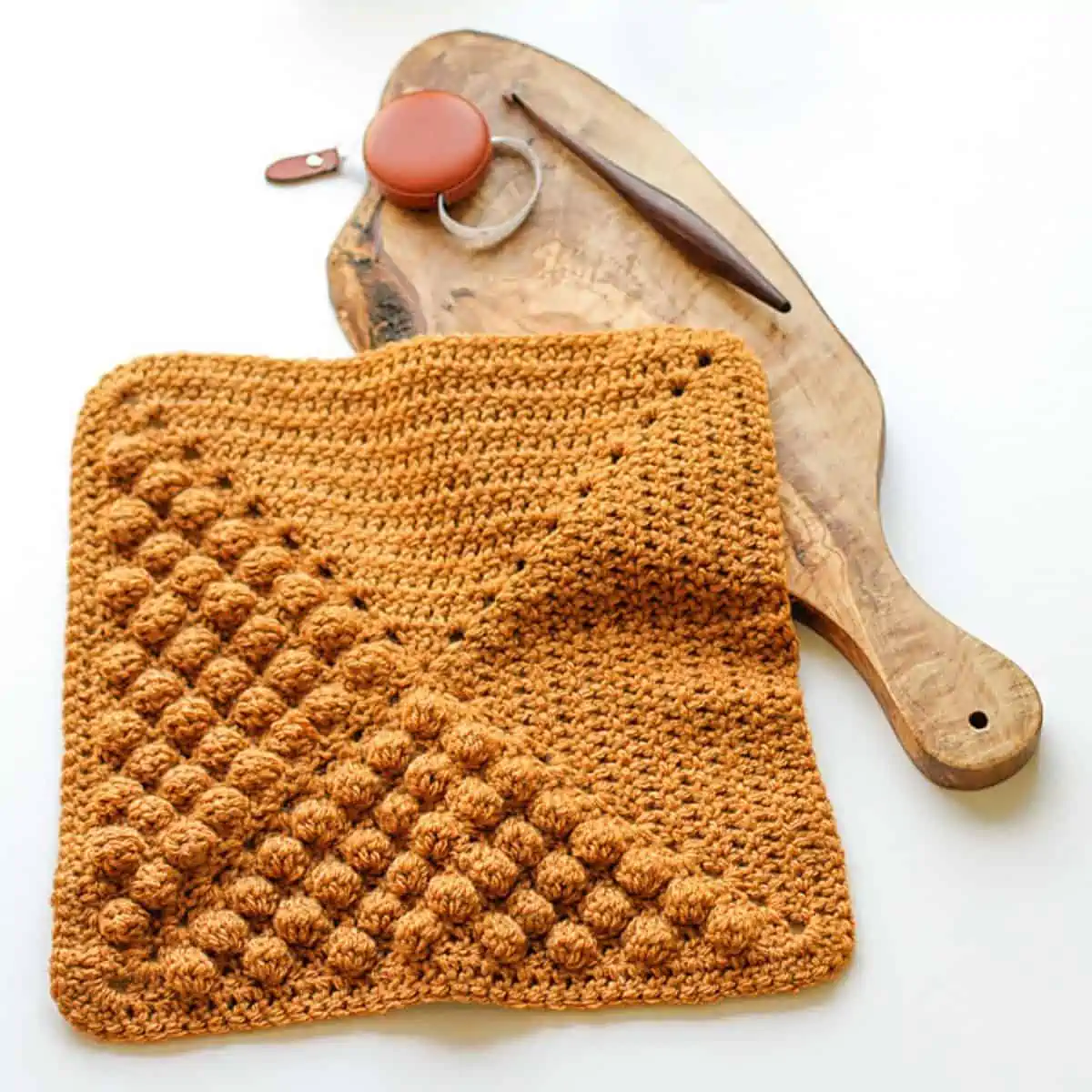 crochet square with bobbles laying on top of a wooden cutting board