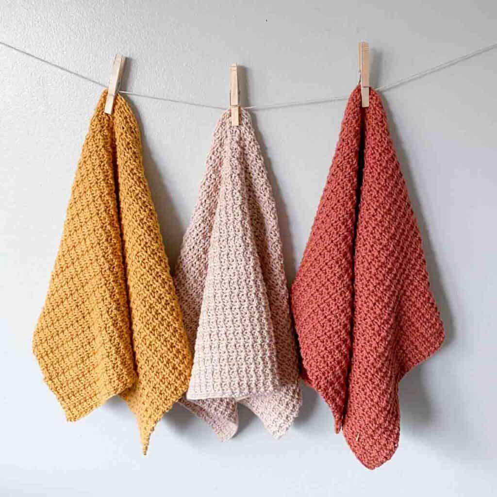 three colorful hand towels crocheted hanging from clothes pins