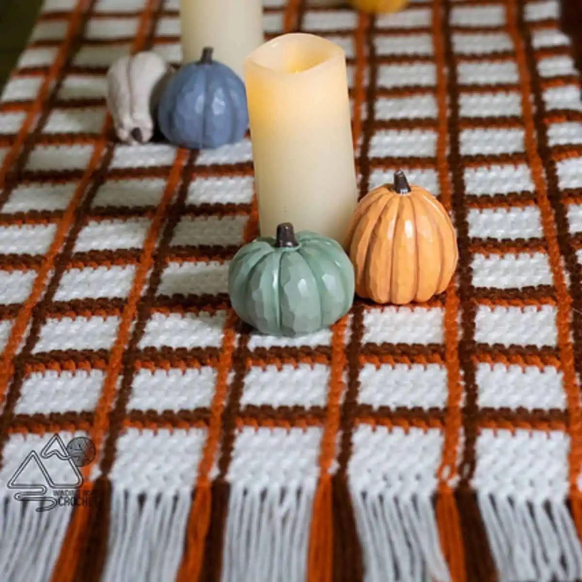 tartan pattern crochet table cloth with candles and pumpkins styled on it