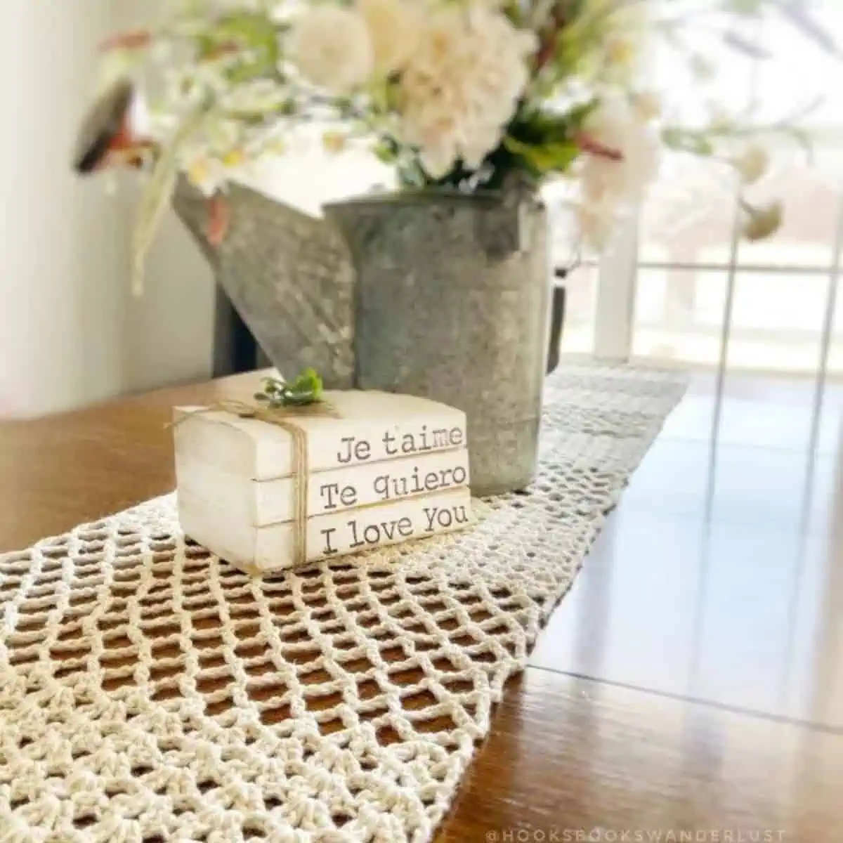 stack of books and a bucket with flowers sitting on an elegant crochet table runner