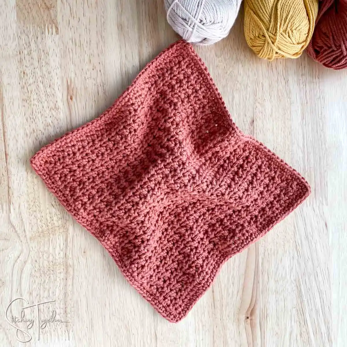 crochet facecloth laying wrinkled on a counter with skeins of yarn barely in the frame