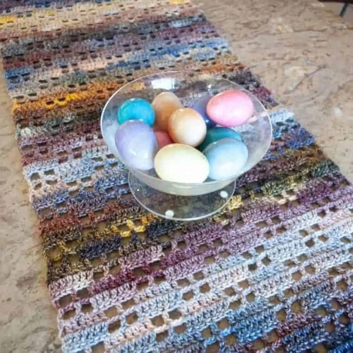 bowl full of easter eggs sitting on top of a crochet table runner