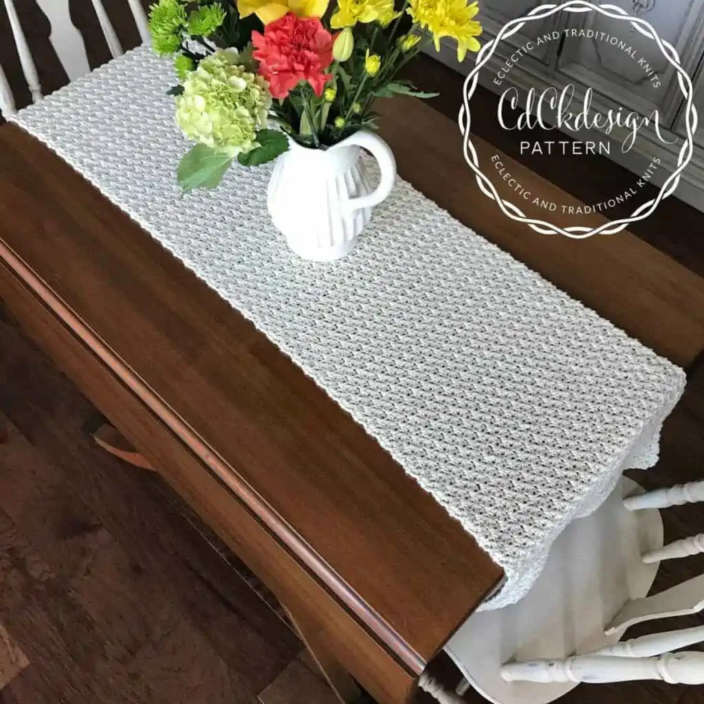 table with a solid crochet table runner and a vase with flowers