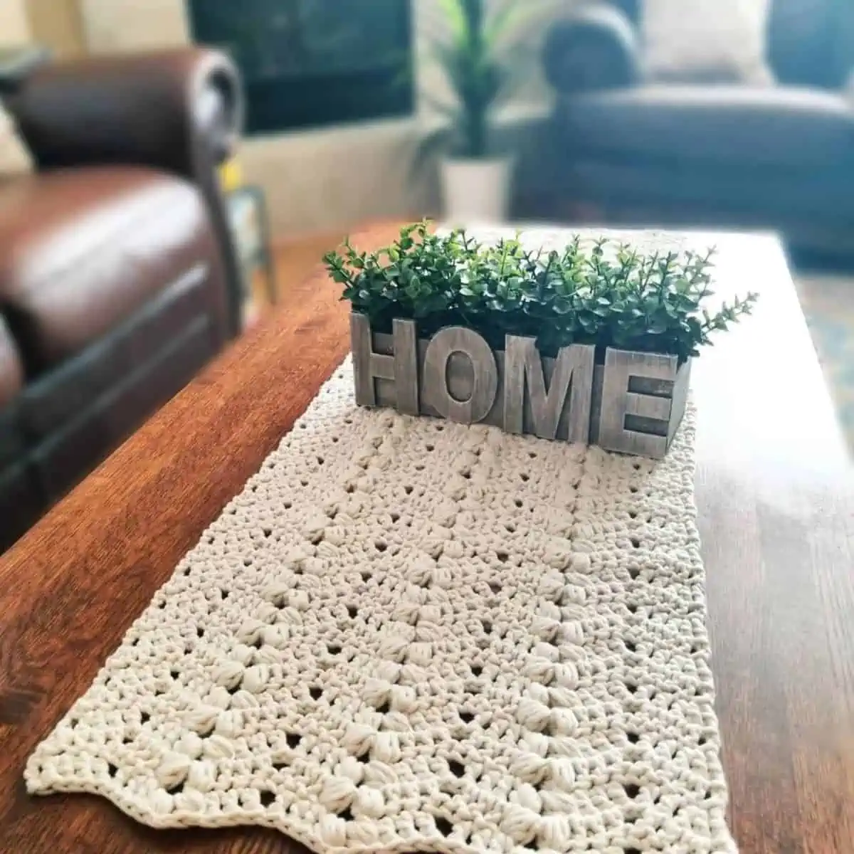 table with a crochet runner and a small grassy vase