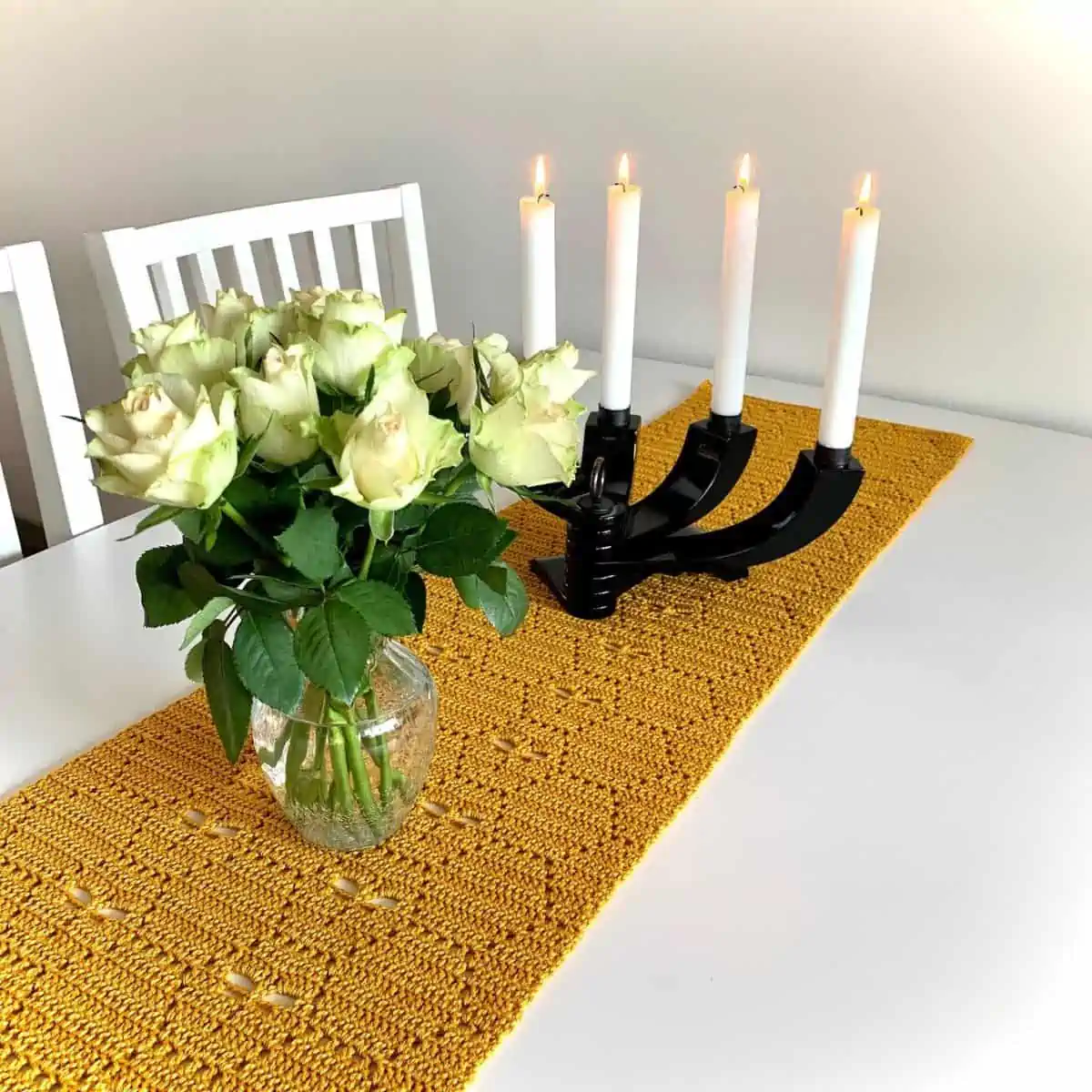 yellow crochet table runner with a hexagon motif laying on a table with candles and flowers on it