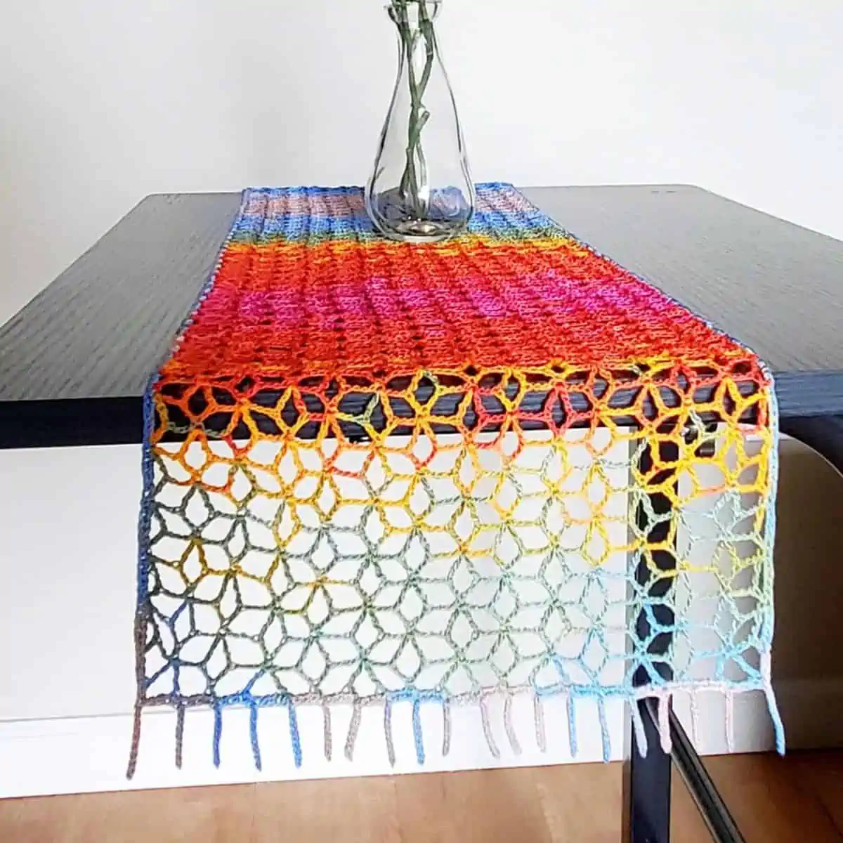 colorful lacy table runner crochet hanging off the side of a black table