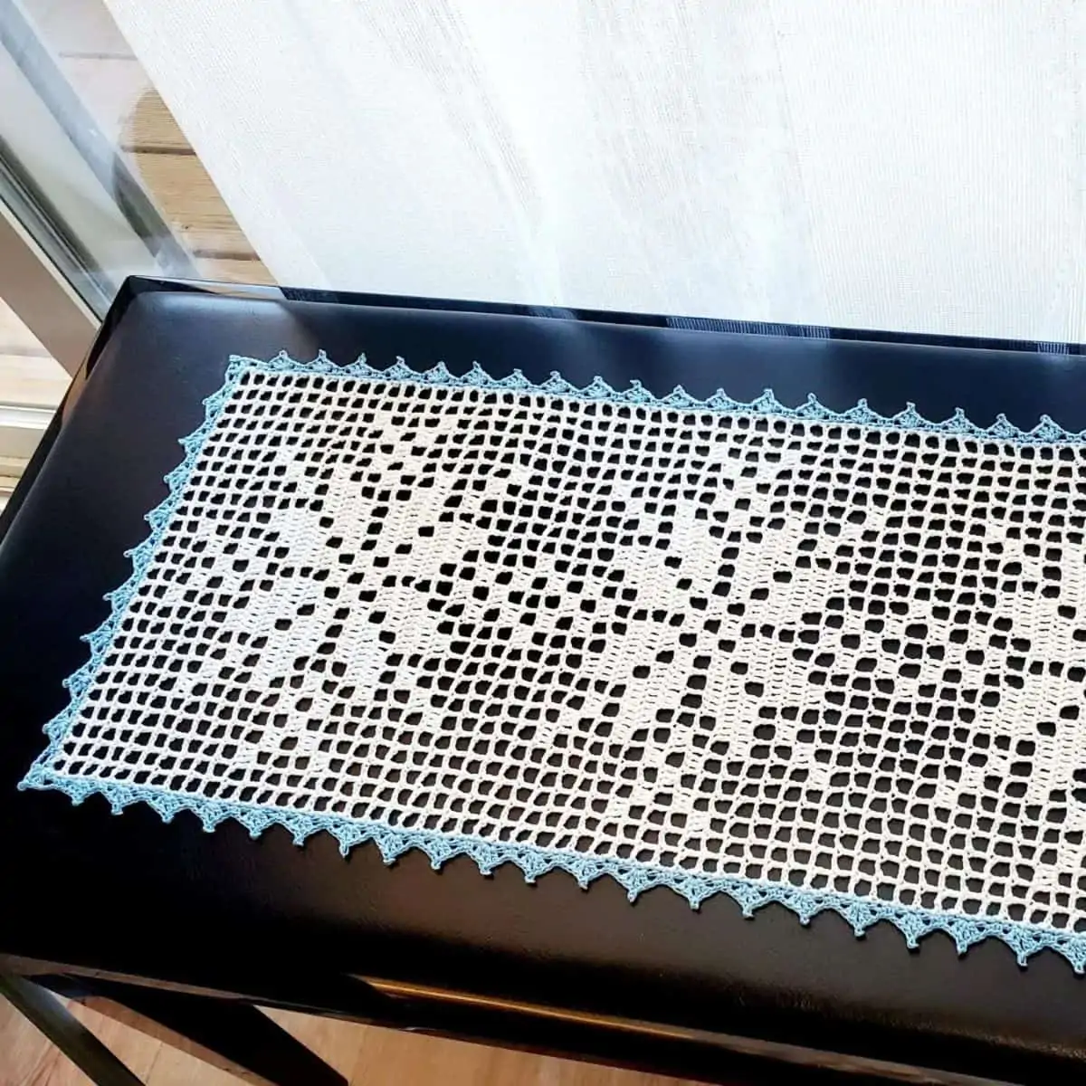 lacy crochet table runner with a snowflake motif sitting on a small black table