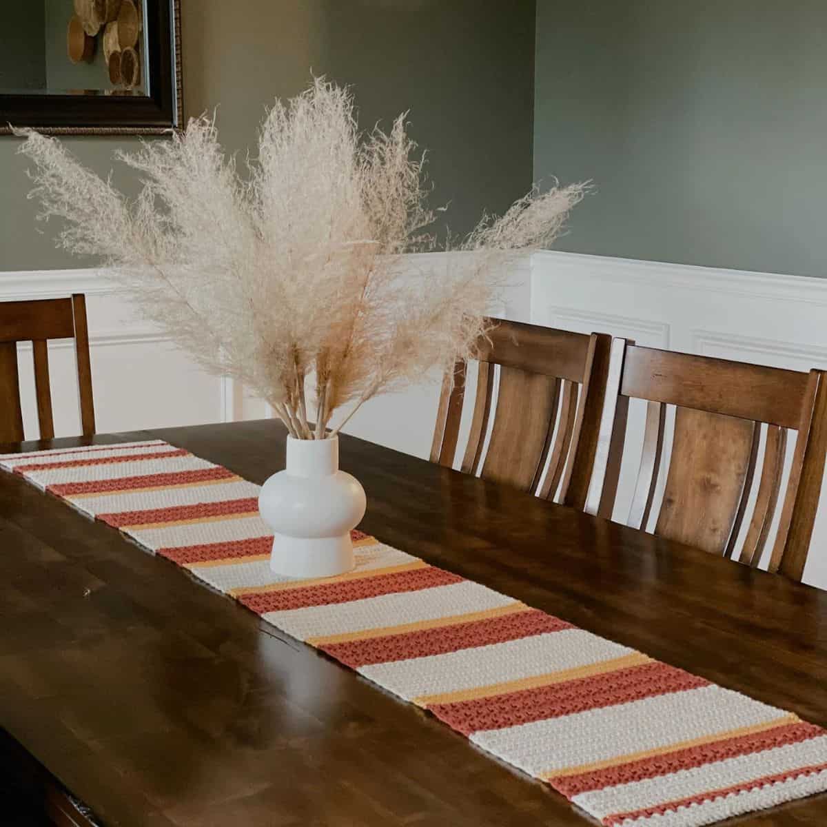 table with a long striped crochet table runner and vase as the centerpiece