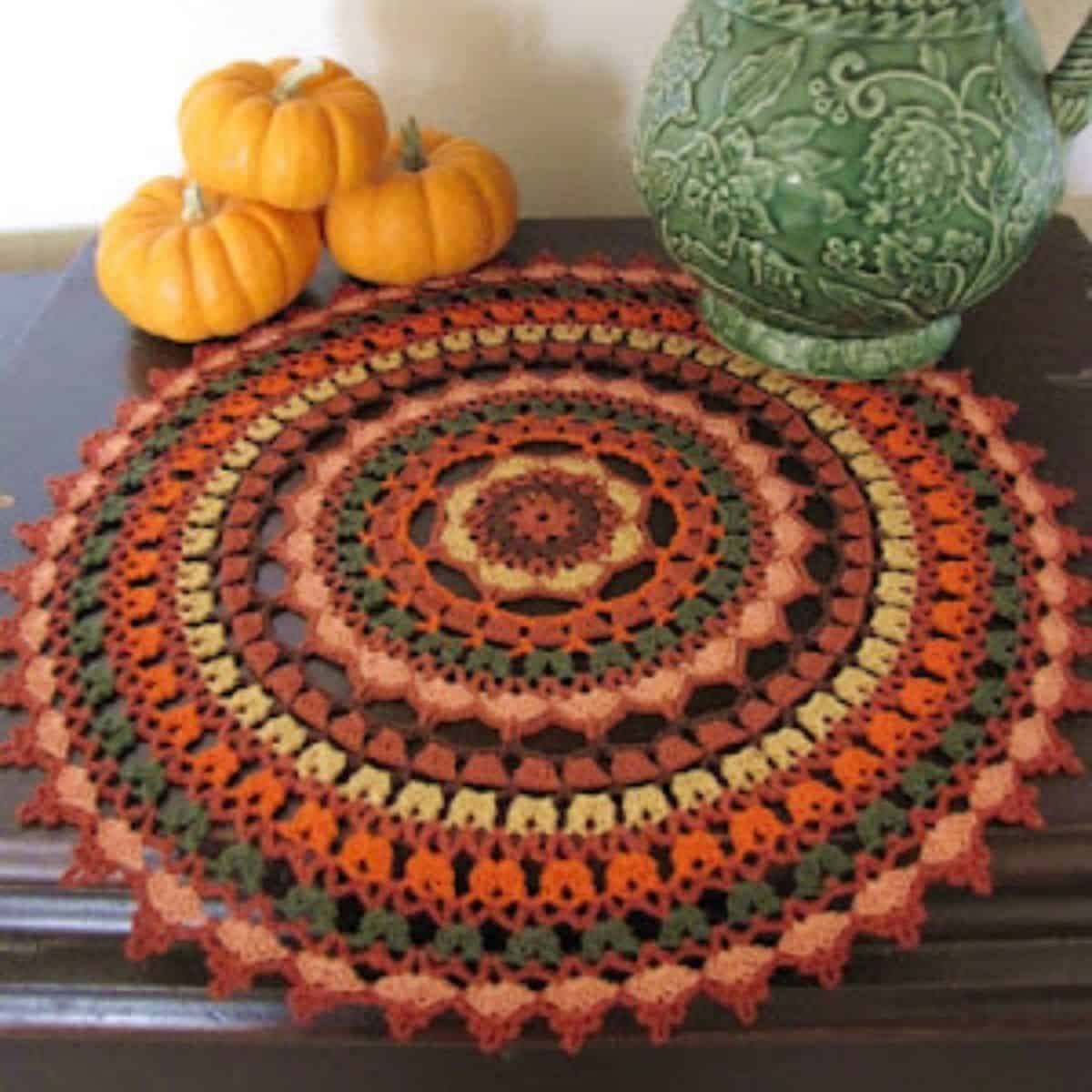 colorful crochet doily displayed on a table with a vase and mini pumpkins