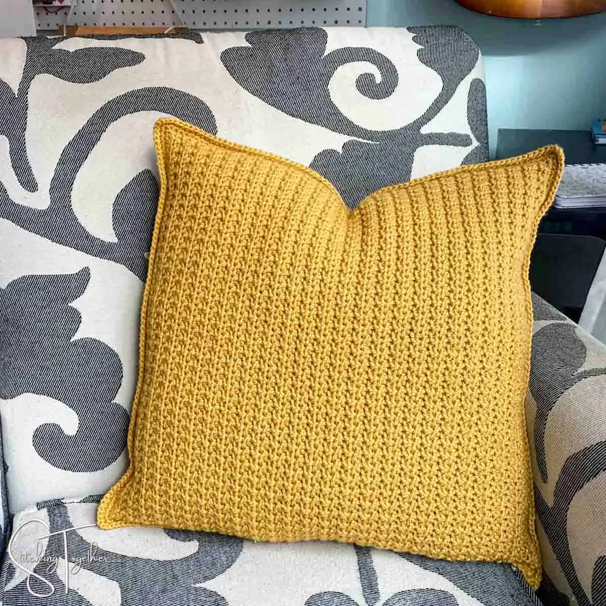 mustard colored crochet pillow on a chair