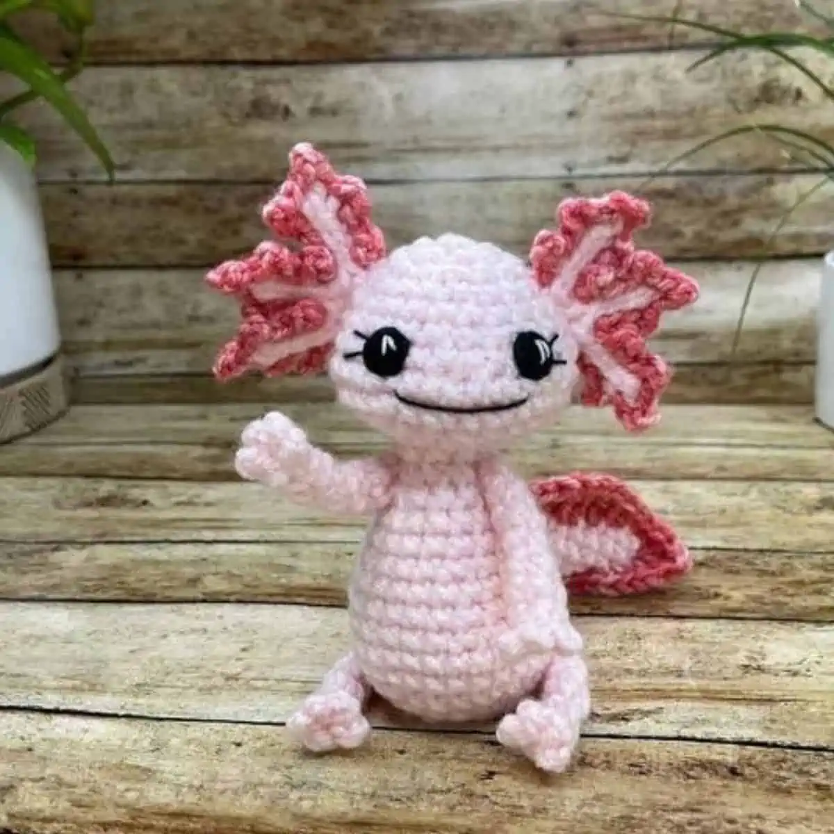 pink crochet axolotl sitting up and waving
