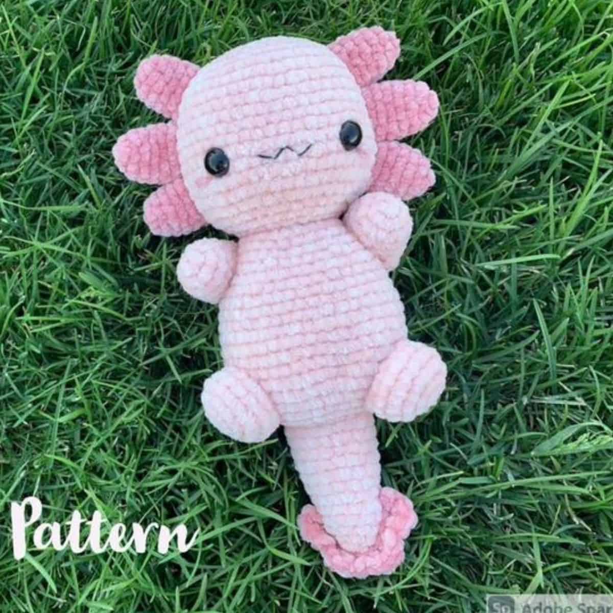 pink crochet axolotl plushie laying on the grass