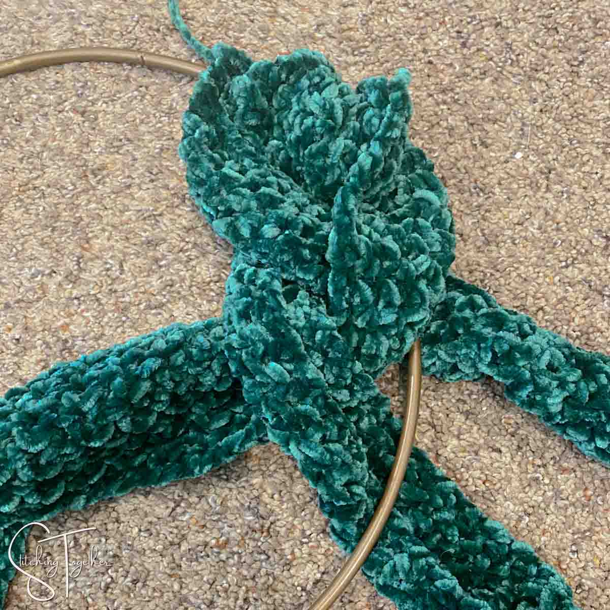 3 strips of green crochet fabric being braided around a metal hoop