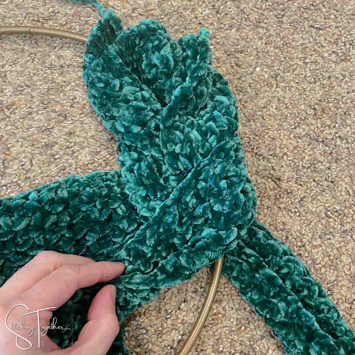 3 strips of green crochet fabric being braided around a metal ring
