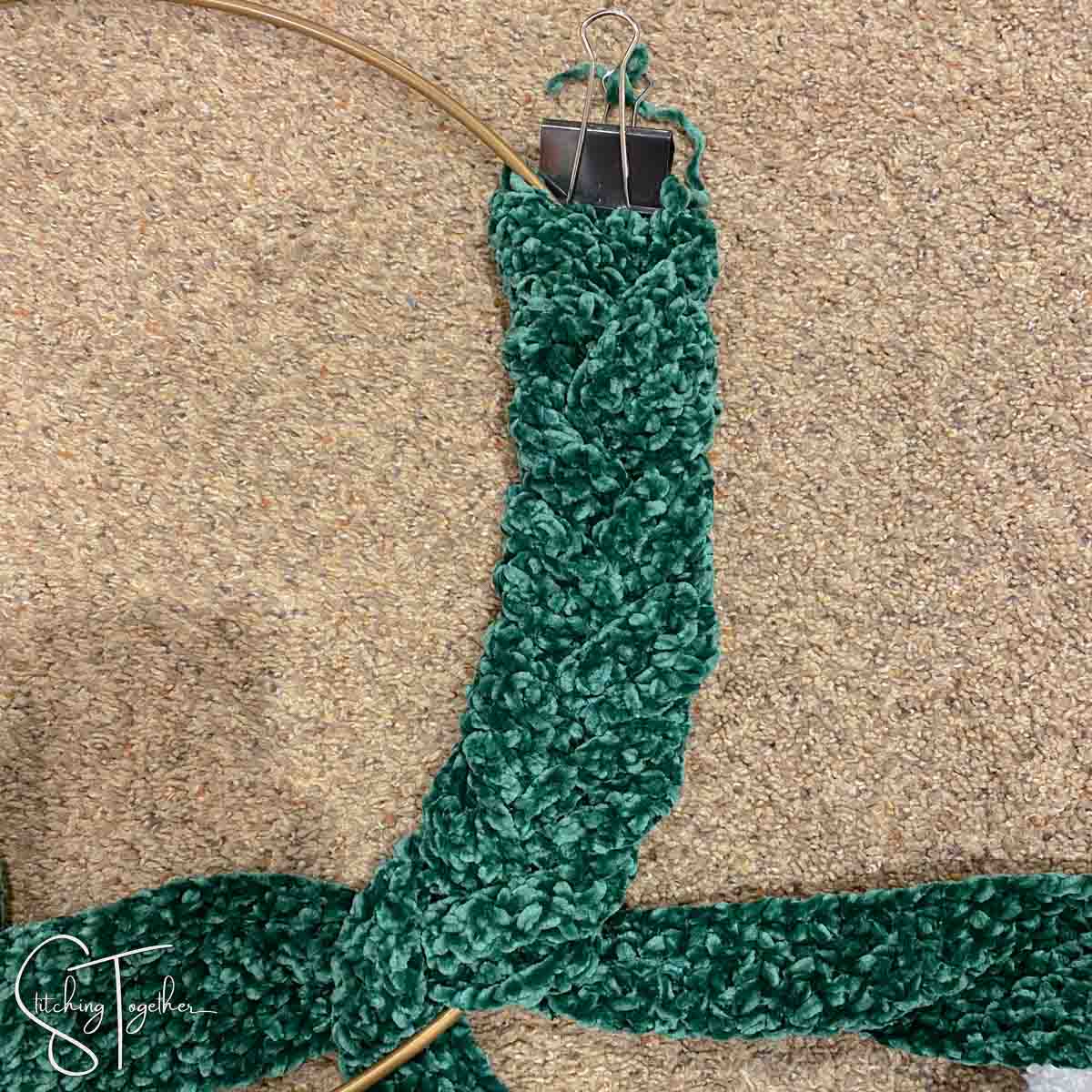 green crochet fabric being braided around a metal hoop