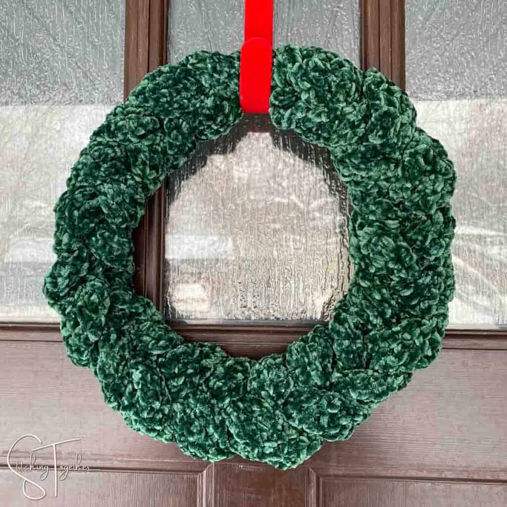 small green crochet wreath hanging on a red wreath hanger
