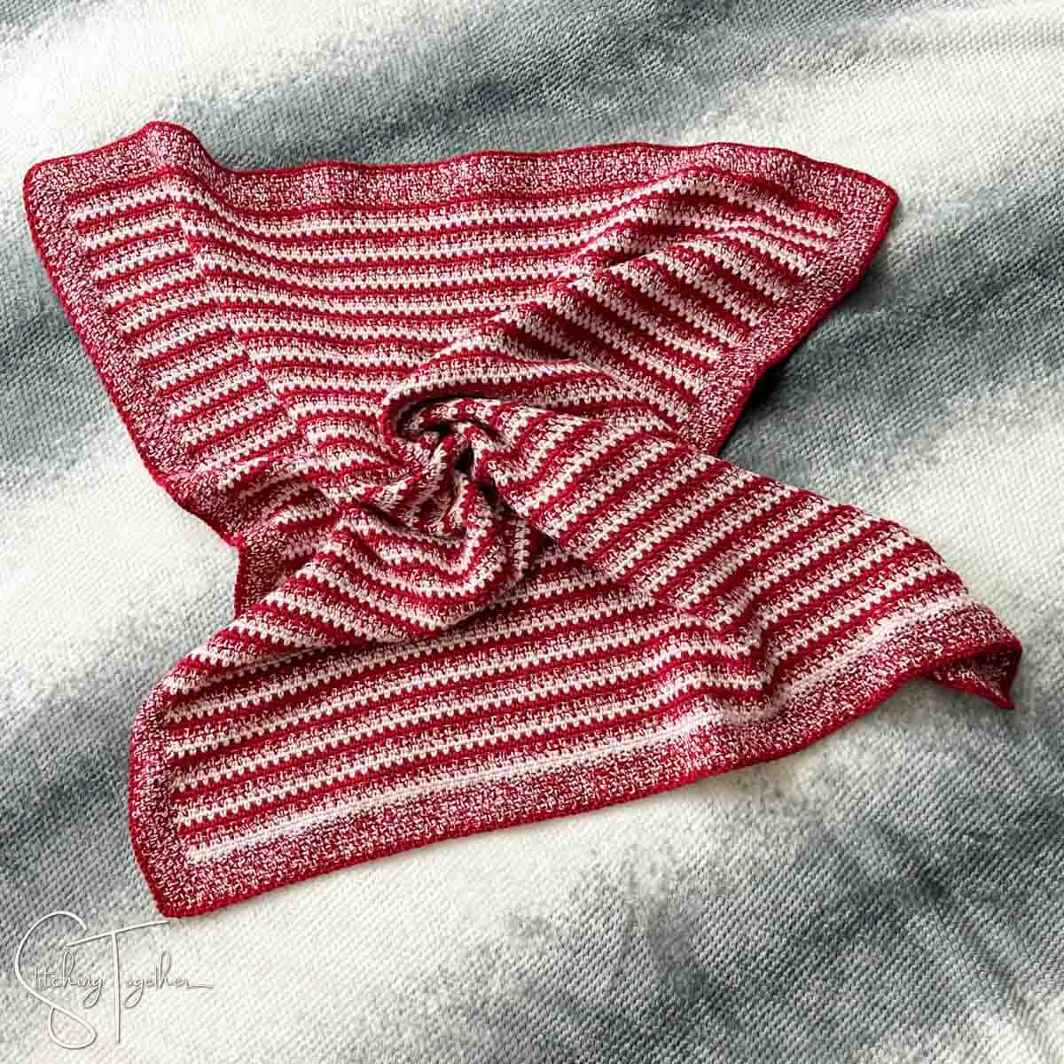 red striped crochet baby blanket slightly crumpled laying on the floor