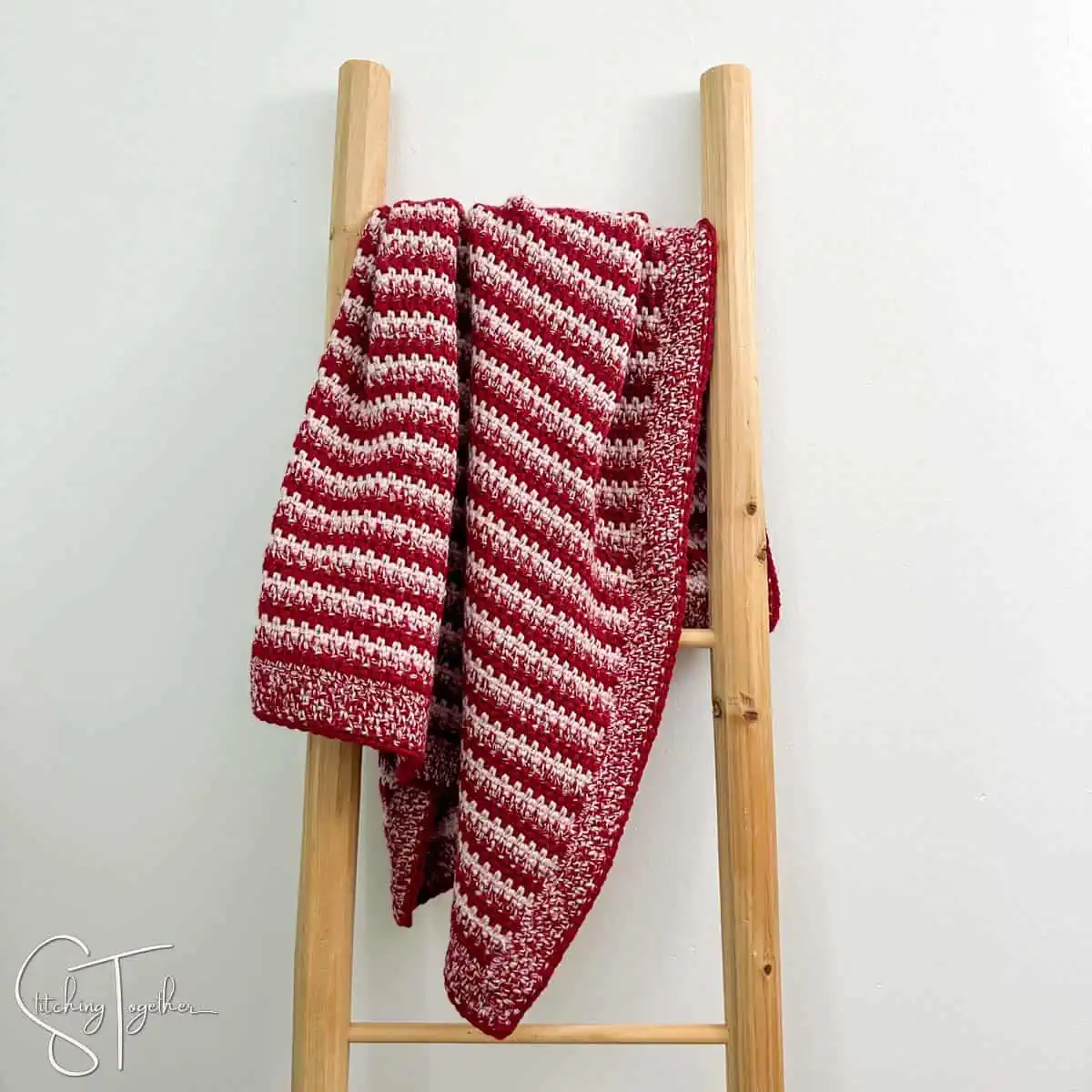 red and pink striped crochet baby blanket draped on a afghan ladder