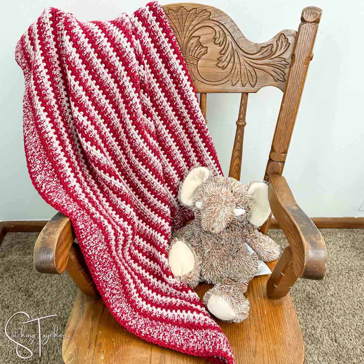 striped crochet baby blanket draped on a small chair with an elephant stuffed animal sitting on the chair