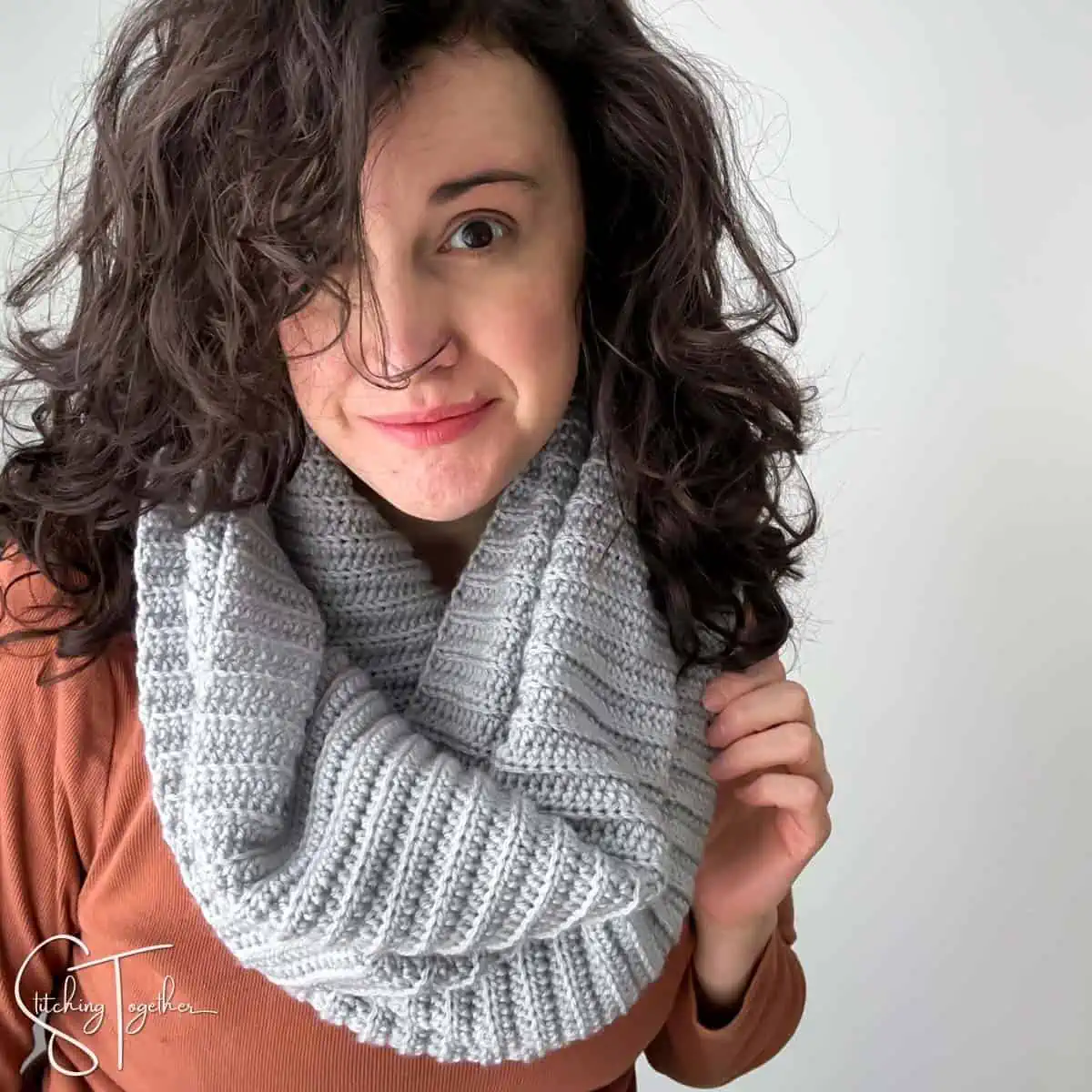 woman wearing an orange shirt and a gray crochet ribbed infinity scarf