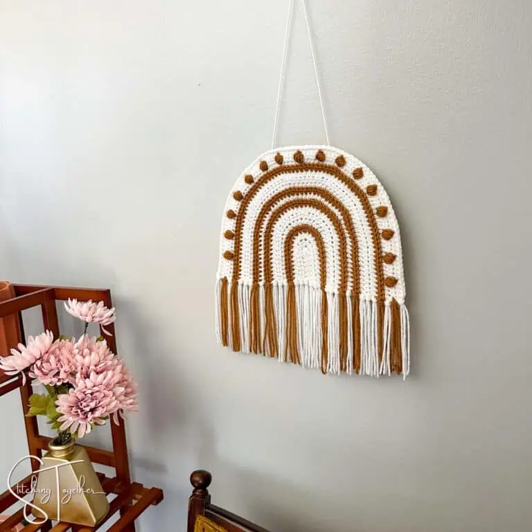 a crochet rainbow wall hanging in 2 colors with fringe on a wall next to some decorations