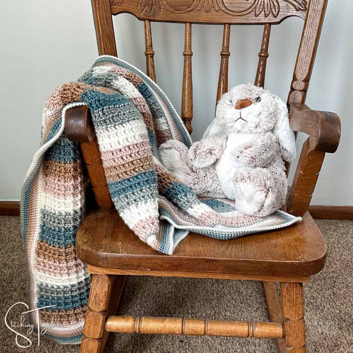 close up of a stuffed rabbit and a striped waffle stitch crochet baby blanket