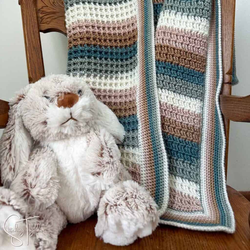 close up of a stuffed rabbit and a striped crochet waffle stitch baby blanket